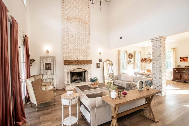 living area featuring a towering ceiling, a fireplace, light wood-style floors, and decorative columns