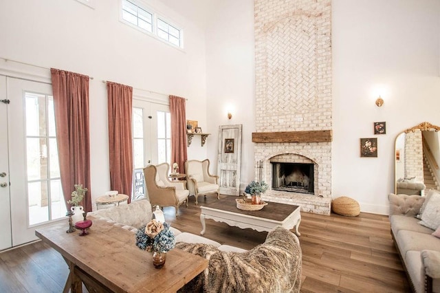 living area featuring a brick fireplace, wood finished floors, baseboards, and a towering ceiling