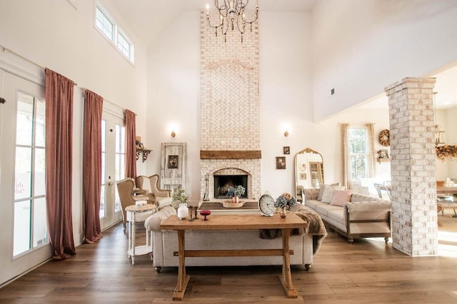 living room with a fireplace, a notable chandelier, wood finished floors, and ornate columns