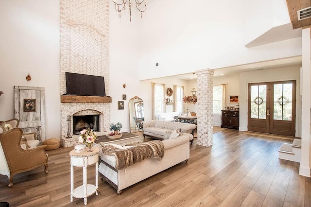 living room featuring visible vents, a fireplace, a high ceiling, wood finished floors, and ornate columns