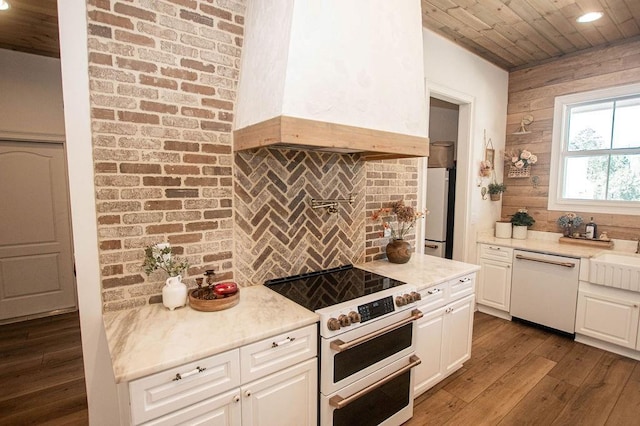 kitchen with white appliances, dark wood-style flooring, custom range hood, white cabinets, and backsplash