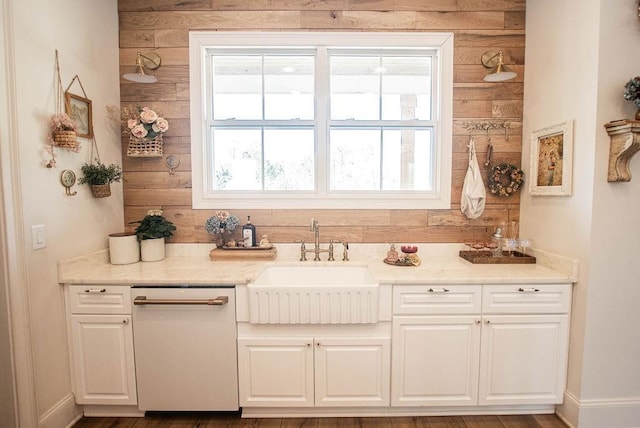 kitchen with baseboards, dishwasher, light stone counters, white cabinetry, and a sink