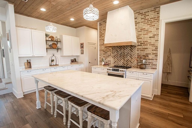 kitchen featuring high end stove, dark wood-type flooring, a kitchen bar, wall chimney exhaust hood, and open shelves