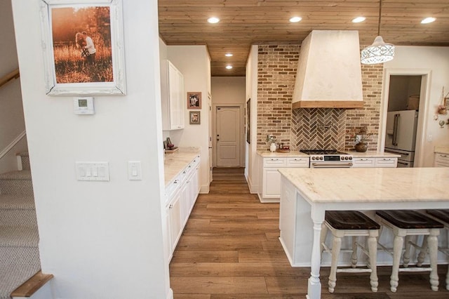 kitchen featuring light wood-style floors, wall chimney exhaust hood, white cabinets, high end appliances, and wood ceiling