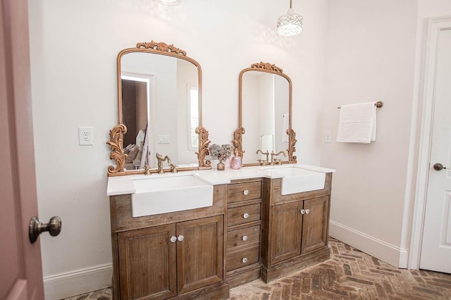 full bath with a sink, baseboards, brick floor, and double vanity