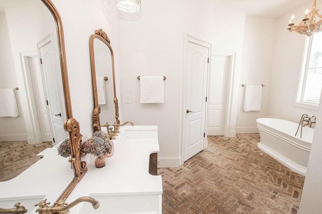 bathroom featuring baseboards, a chandelier, a freestanding bath, brick floor, and vanity