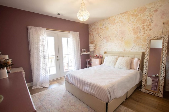 bedroom featuring access to exterior, visible vents, wallpapered walls, french doors, and wood finished floors