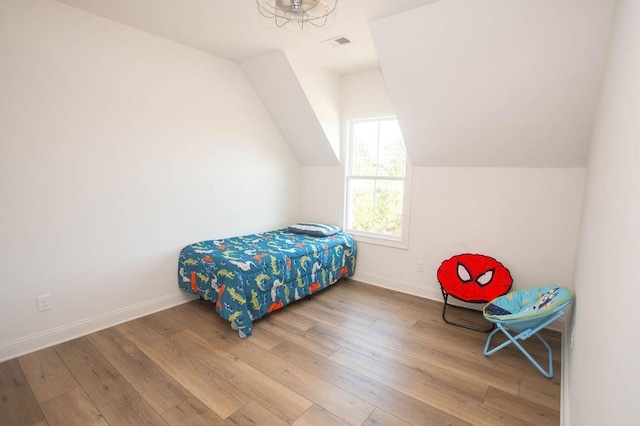 bedroom with visible vents, lofted ceiling, baseboards, and wood finished floors