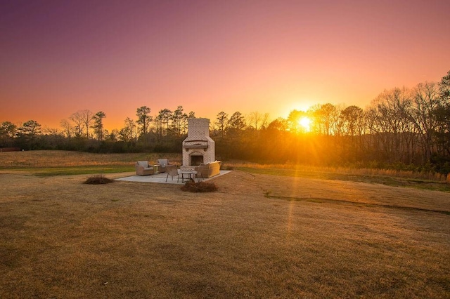 playground at dusk with a patio area, a yard, and an outdoor fireplace