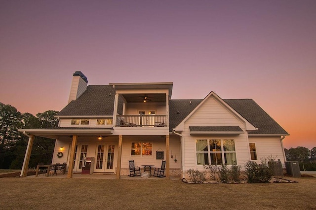 rear view of property featuring french doors, a chimney, a yard, a balcony, and a patio