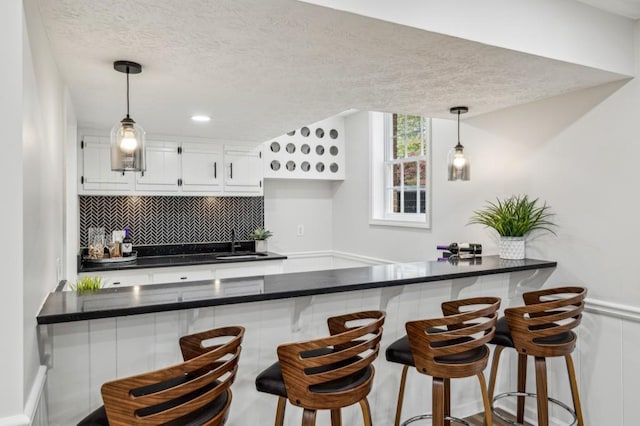6124 Kings Mountain Ct, Stone Mountain, GA 30087 - kitchen with a textured ceiling, dark countertops, tasteful backsplash, white cabinetry, and a sink