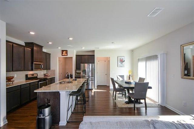 kitchen with sink, appliances with stainless steel finishes, a kitchen bar, a center island with sink, and dark hardwood / wood-style flooring