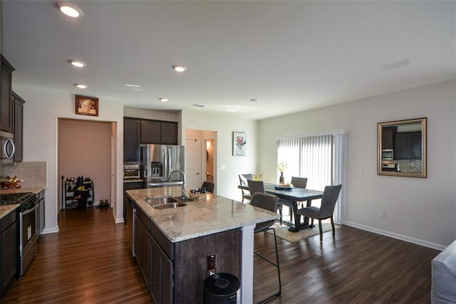 kitchen with dark brown cabinetry, appliances with stainless steel finishes, sink, and an island with sink