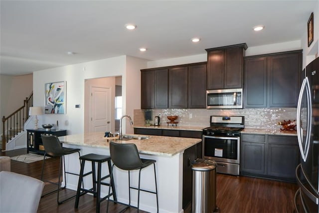 kitchen featuring light stone countertops, an island with sink, appliances with stainless steel finishes, and sink