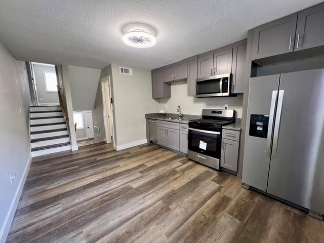 kitchen with dark hardwood / wood-style floors, gray cabinetry, sink, appliances with stainless steel finishes, and a textured ceiling