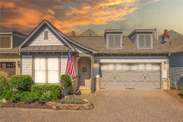 view of front of property featuring an attached garage, a standing seam roof, decorative driveway, and brick siding