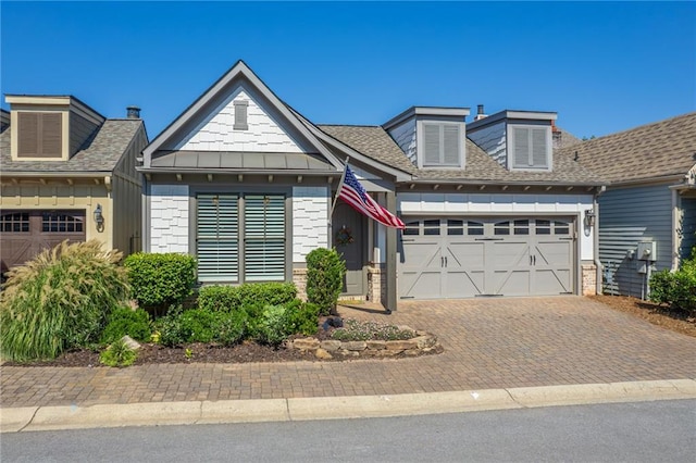 view of front of house featuring decorative driveway, roof with shingles, brick siding, board and batten siding, and a garage