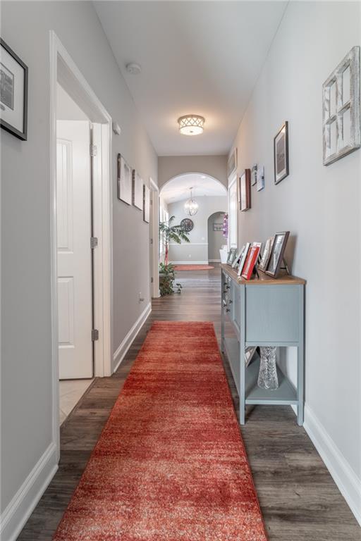 hall featuring dark wood-style floors, arched walkways, and baseboards