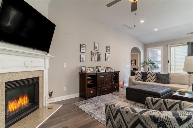 living area with baseboards, arched walkways, dark wood-style floors, vaulted ceiling, and a high end fireplace