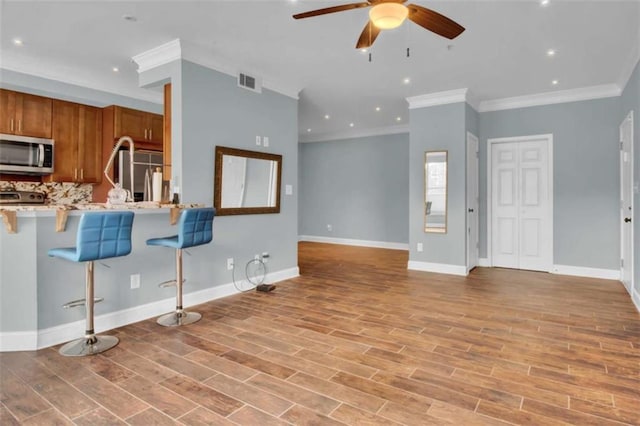 200 Renaissance Pkwy NE Unit 304, Atlanta, GA 30308 - kitchen featuring appliances with stainless steel finishes, brown cabinets, ornamental molding, a ceiling fan, and a kitchen breakfast bar