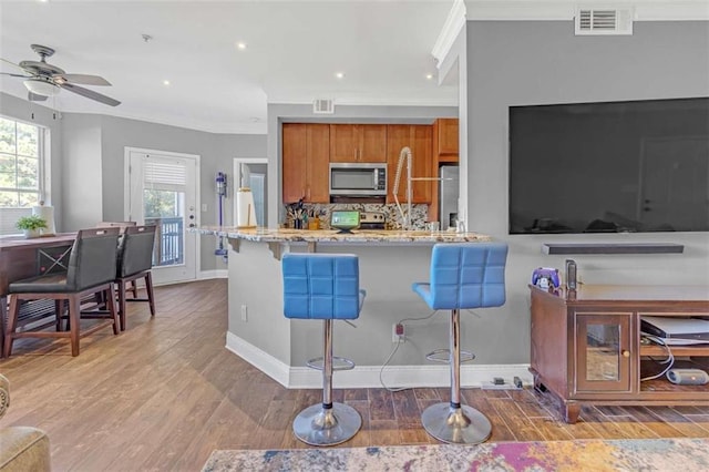 200 Renaissance Pkwy NE Unit 304, Atlanta, GA 30308 - kitchen with stainless steel microwave, brown cabinets, crown molding, a ceiling fan, and light wood-style flooring