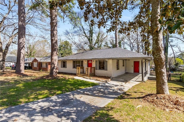 ranch-style home featuring brick siding, a front yard, an attached carport, and driveway