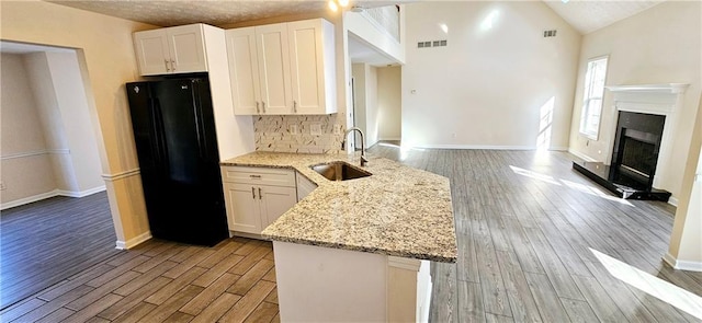 kitchen featuring light stone countertops, black fridge, sink, white cabinets, and light hardwood / wood-style floors