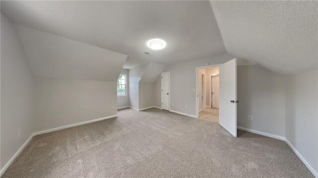 additional living space with visible vents, lofted ceiling, baseboards, a textured ceiling, and carpet