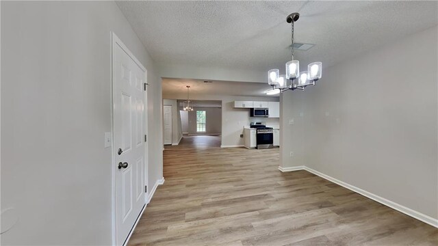 interior space featuring light wood-style floors, baseboards, a textured ceiling, and a notable chandelier