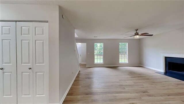 unfurnished living room with a ceiling fan, baseboards, light wood finished floors, and a fireplace