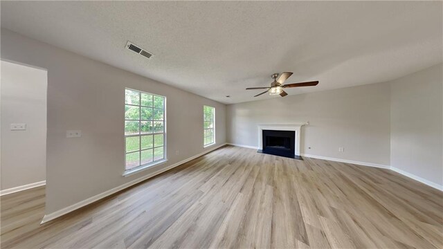 unfurnished living room featuring a ceiling fan, visible vents, a fireplace with flush hearth, light wood-type flooring, and baseboards