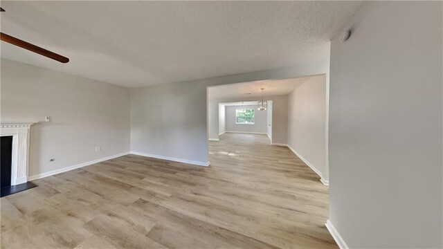 unfurnished living room with baseboards, a fireplace with raised hearth, ceiling fan with notable chandelier, and light wood-type flooring