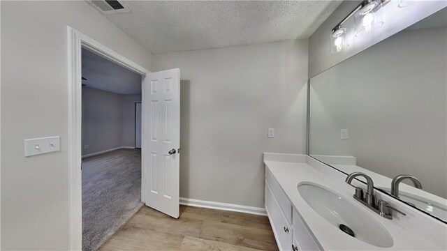bathroom featuring visible vents, vanity, wood finished floors, baseboards, and a textured ceiling