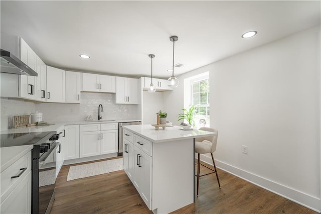 kitchen featuring stainless steel appliances, a kitchen island, dark wood-type flooring, pendant lighting, and white cabinetry