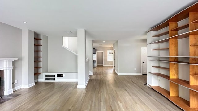 unfurnished living room featuring built in features, a fireplace, baseboards, and wood finished floors