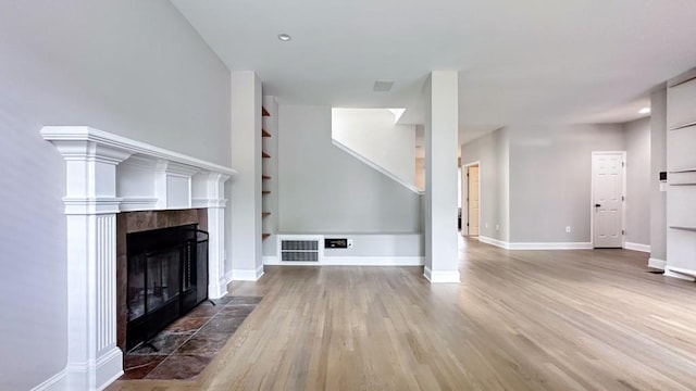 unfurnished living room with baseboards, visible vents, a tiled fireplace, and wood finished floors