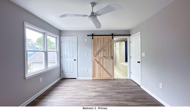 unfurnished bedroom featuring a barn door, a ceiling fan, connected bathroom, wood finished floors, and baseboards