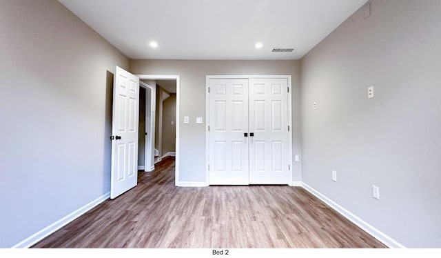 unfurnished bedroom with baseboards, a closet, visible vents, and wood finished floors