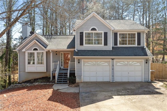 tri-level home featuring a garage, a shingled roof, driveway, and fence