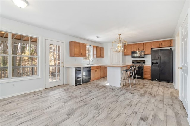 kitchen featuring a kitchen island, a kitchen bar, light countertops, black appliances, and a sink