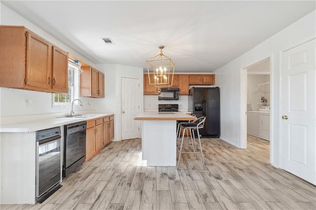 kitchen featuring black appliances, a breakfast bar, a sink, light wood-style floors, and washing machine and clothes dryer