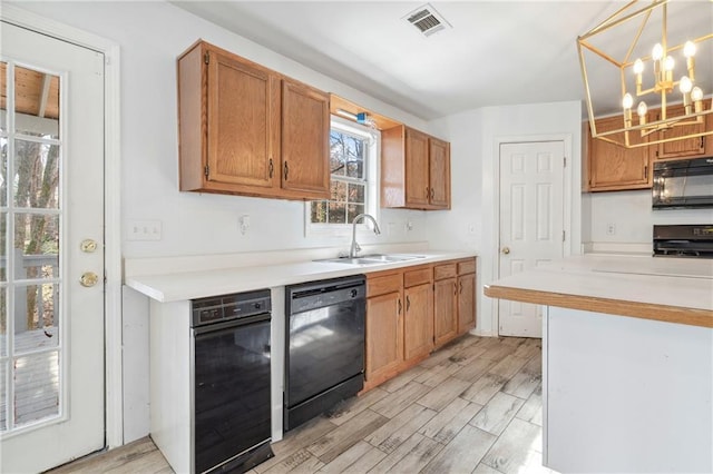 kitchen with visible vents, light wood finished floors, black appliances, a sink, and light countertops