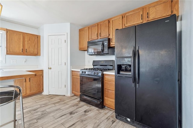 kitchen featuring black appliances, light countertops, light wood-type flooring, and brown cabinets