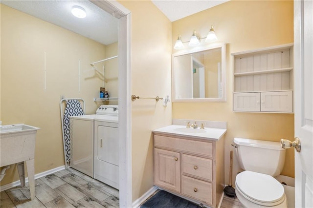 bathroom with baseboards, toilet, wood finished floors, independent washer and dryer, and vanity