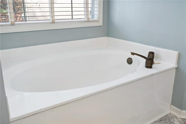 bathroom featuring marble finish floor and a bath