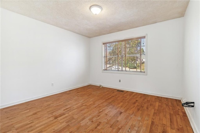 spare room with visible vents, a textured ceiling, light wood-type flooring, and baseboards