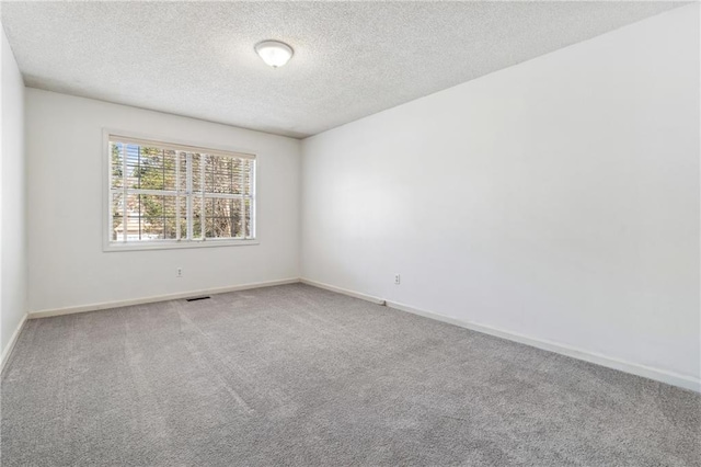 carpeted empty room featuring visible vents, a textured ceiling, and baseboards