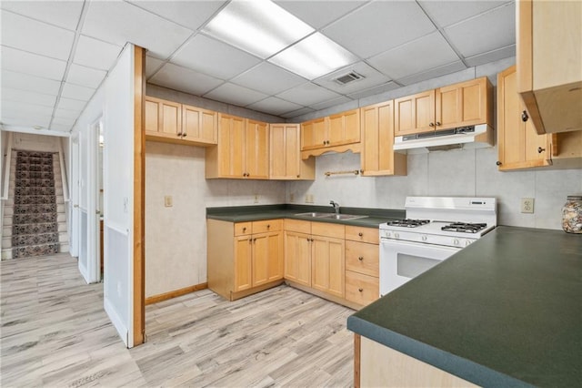 kitchen featuring under cabinet range hood, white range with gas cooktop, dark countertops, and a sink