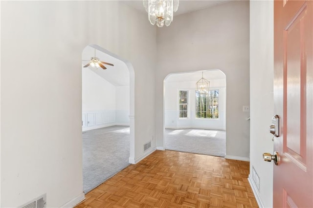 foyer entrance with arched walkways, visible vents, light colored carpet, and a towering ceiling