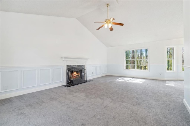 unfurnished living room featuring high vaulted ceiling, a premium fireplace, ceiling fan, wainscoting, and carpet flooring